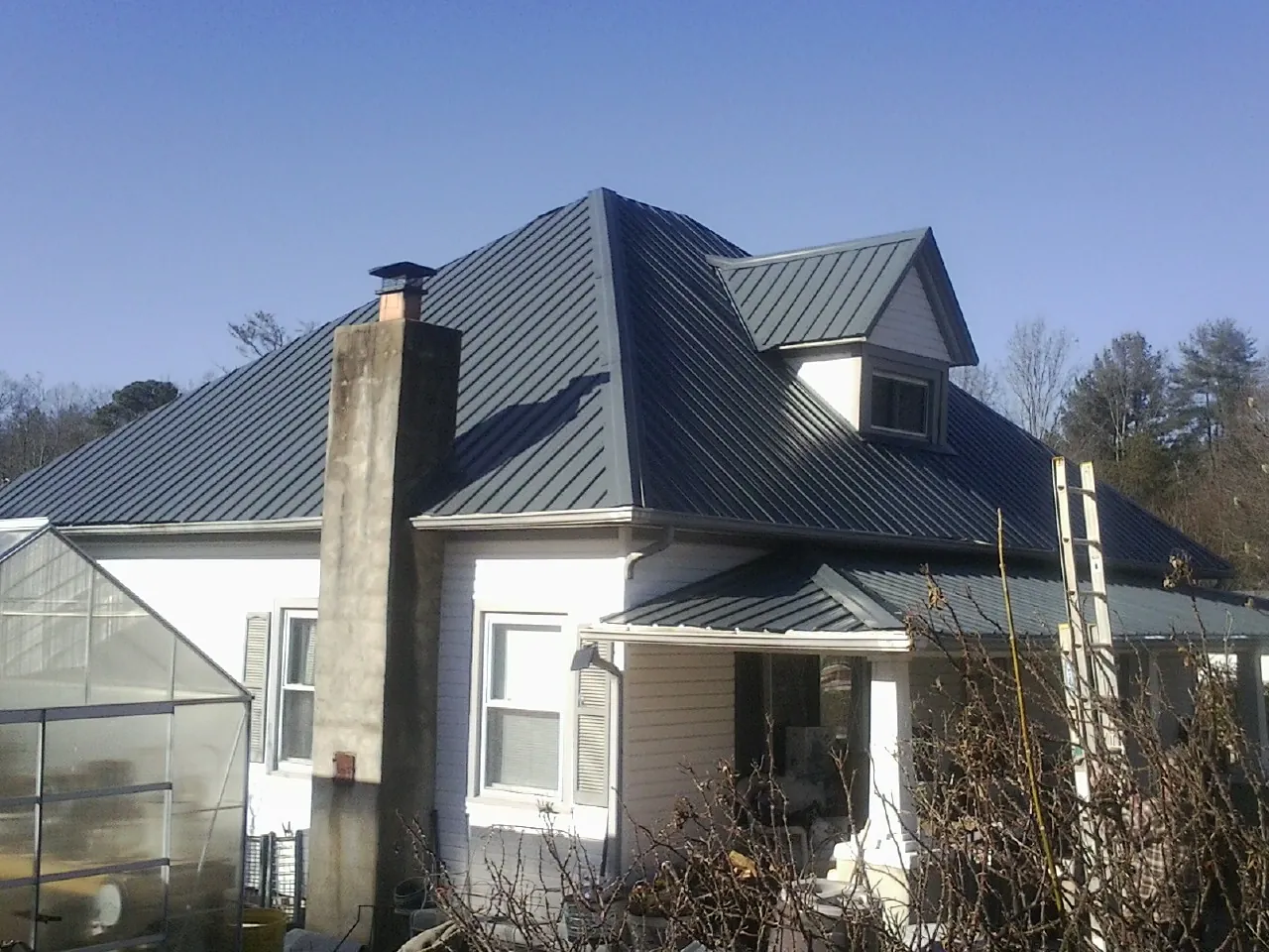 Dark blue standing seam metal roof on a white farmhouse with dormer — Slate & Tile Roof Repair by Roofing Brothers in Solen