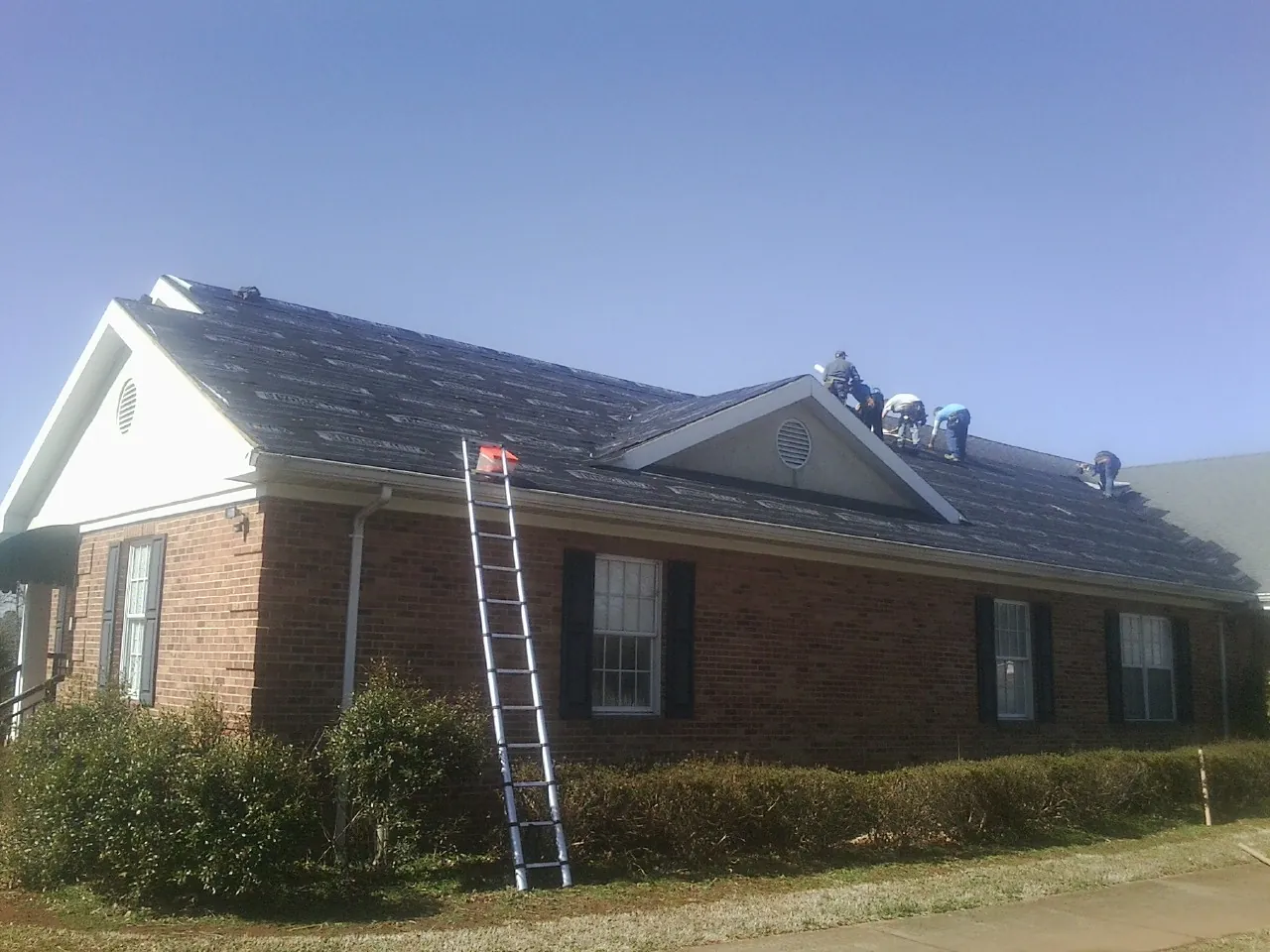 Crew tearing shingles off a brick ranch roof with a ladder set — Emergency Roof Repair work by our crew in Solen