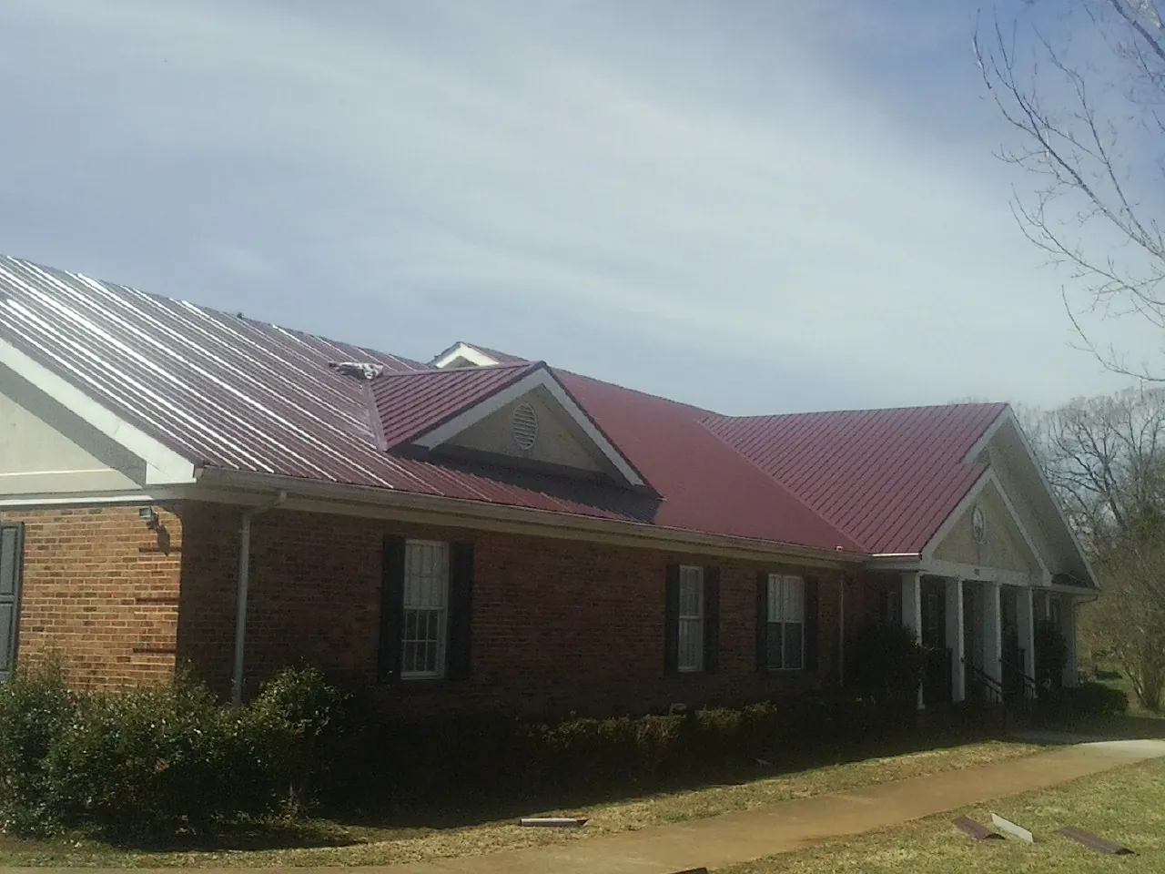 Red metal roof with gabled entries on a long brick building, from a Hail Damage Roof Repair job in Solen