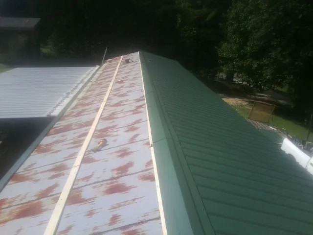 Old rusted panels beside newly installed green metal roofing — Wind Damage Roof Repair by Roofing Brothers in Solen