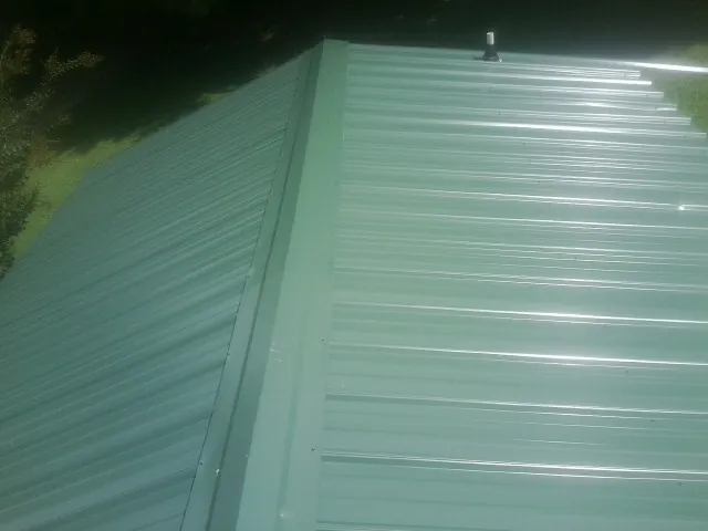 New green metal panels meeting at the ridge of a roof — Flat Roof Repair work by our crew in Solen