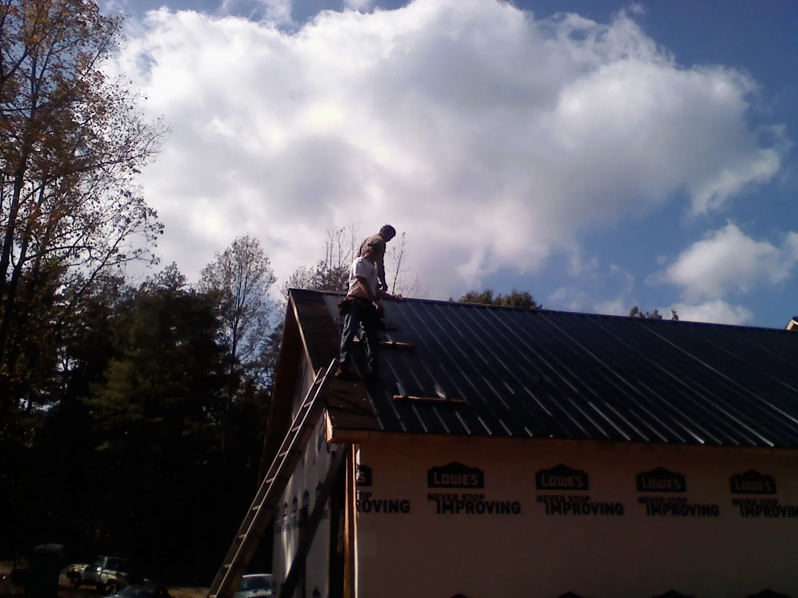 Roofer fastening dark metal panels high against a cloudy sky, from a Roof Inspection job in Solen